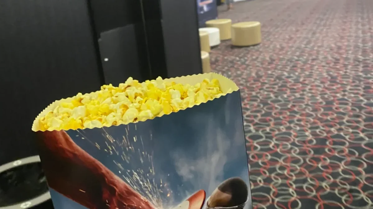 fotografie popcornu v ruce a v pozadí sál kina