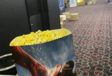 fotografie popcornu v ruce a v pozadí sál kina