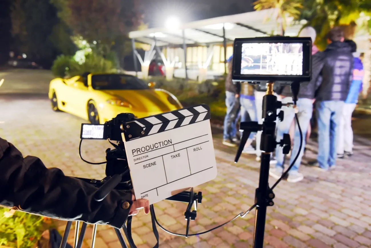 Shutterstock_2367437137 | TVGURU.cz natáčení filmu, kamera, klapka, v pozadí sportovní auto