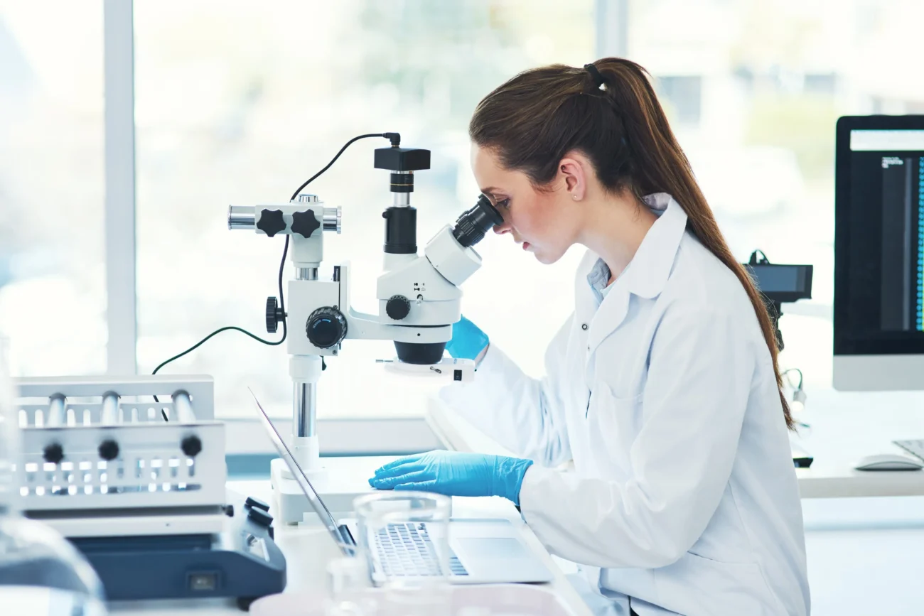 shutterstock_2507089649 1 | TVGURU.cz Žena v laboratoři kouká do mikroskopu.