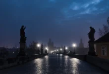 Pražský Karlův most v mlžné tmavé noci; lucerny svítí, tajemná až strašidelná atmosféra