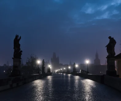 Pražský Karlův most v mlžné tmavé noci; lucerny svítí, tajemná až strašidelná atmosféra