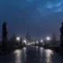 Pražský Karlův most v mlžné tmavé noci; lucerny svítí, tajemná až strašidelná atmosféra