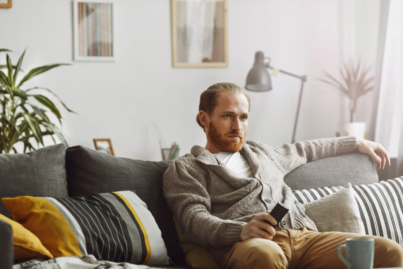 shutterstock_1555433459-2 | TVGURU.cz Muž sedí na gauči.
