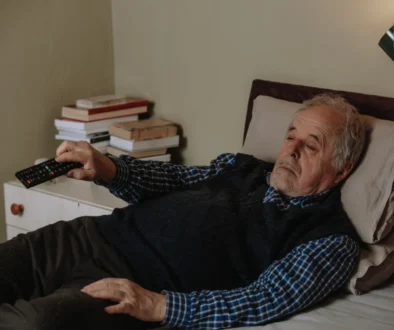 shutterstock_1936494367-2 Muž leží na posteli s ovladačem v ruce.