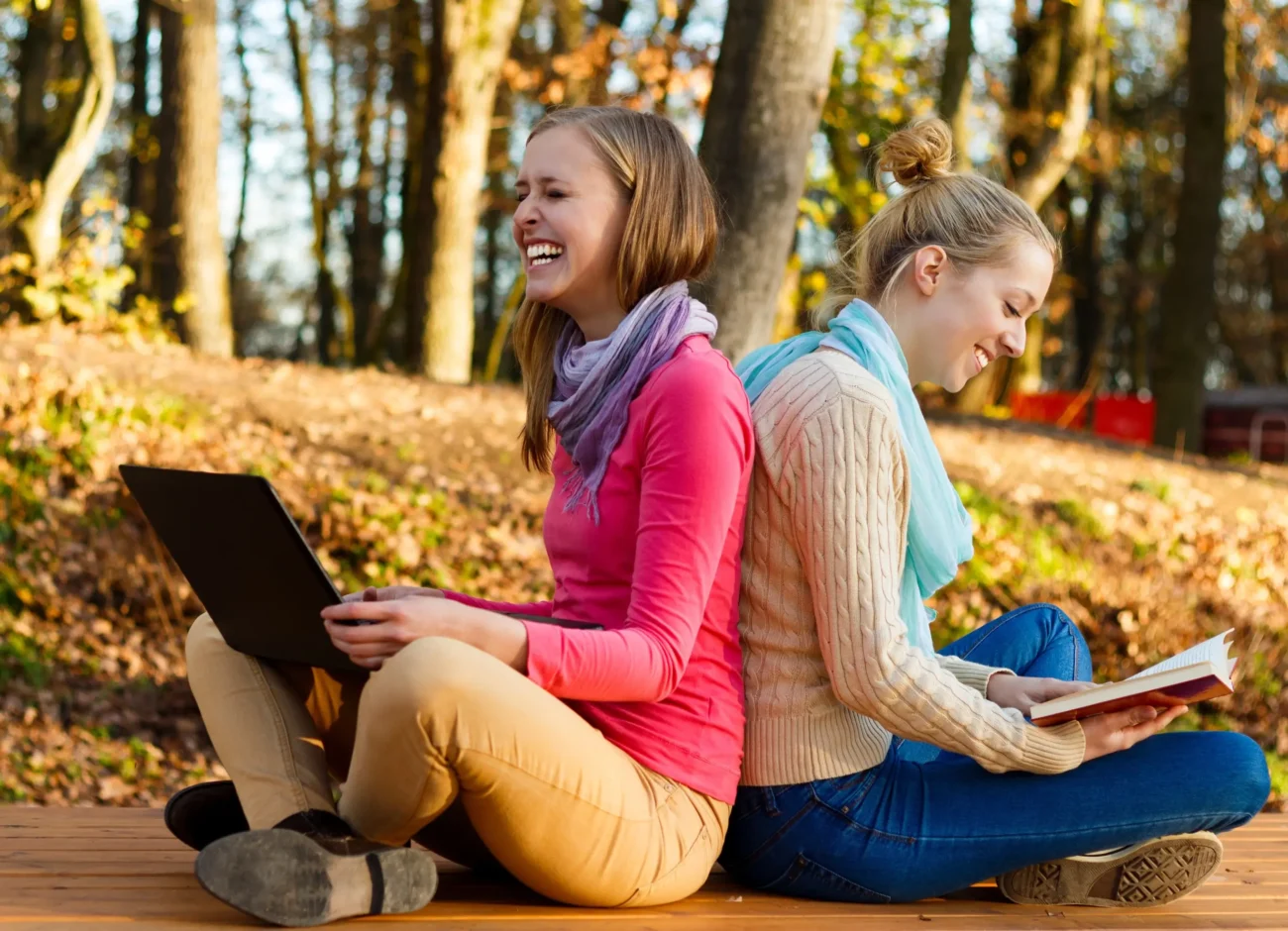 Dvě ženy o sebe sedí opřené a čtou si. 