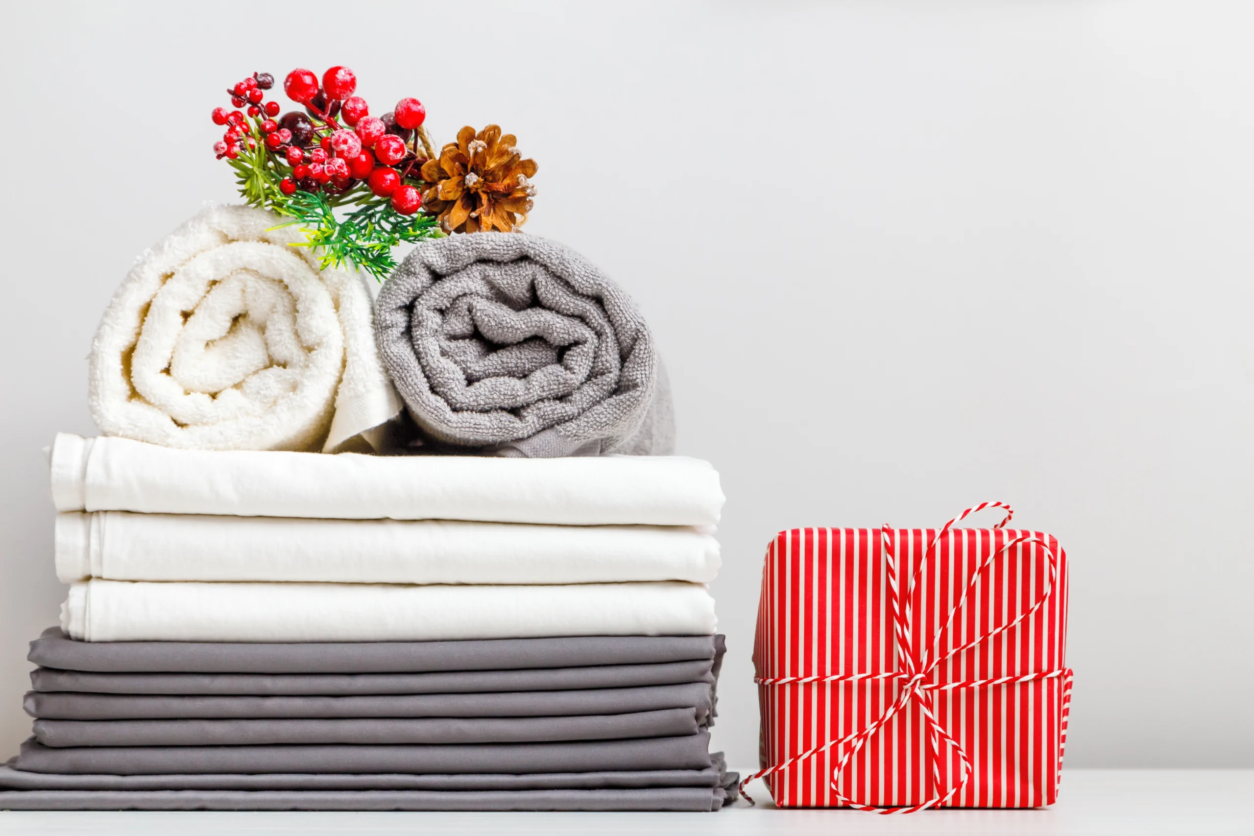 shutterstock_2201342691 | TVGURU.cz Složená prostěradla a ručníky ozdobené vánoční dekorací na stolku