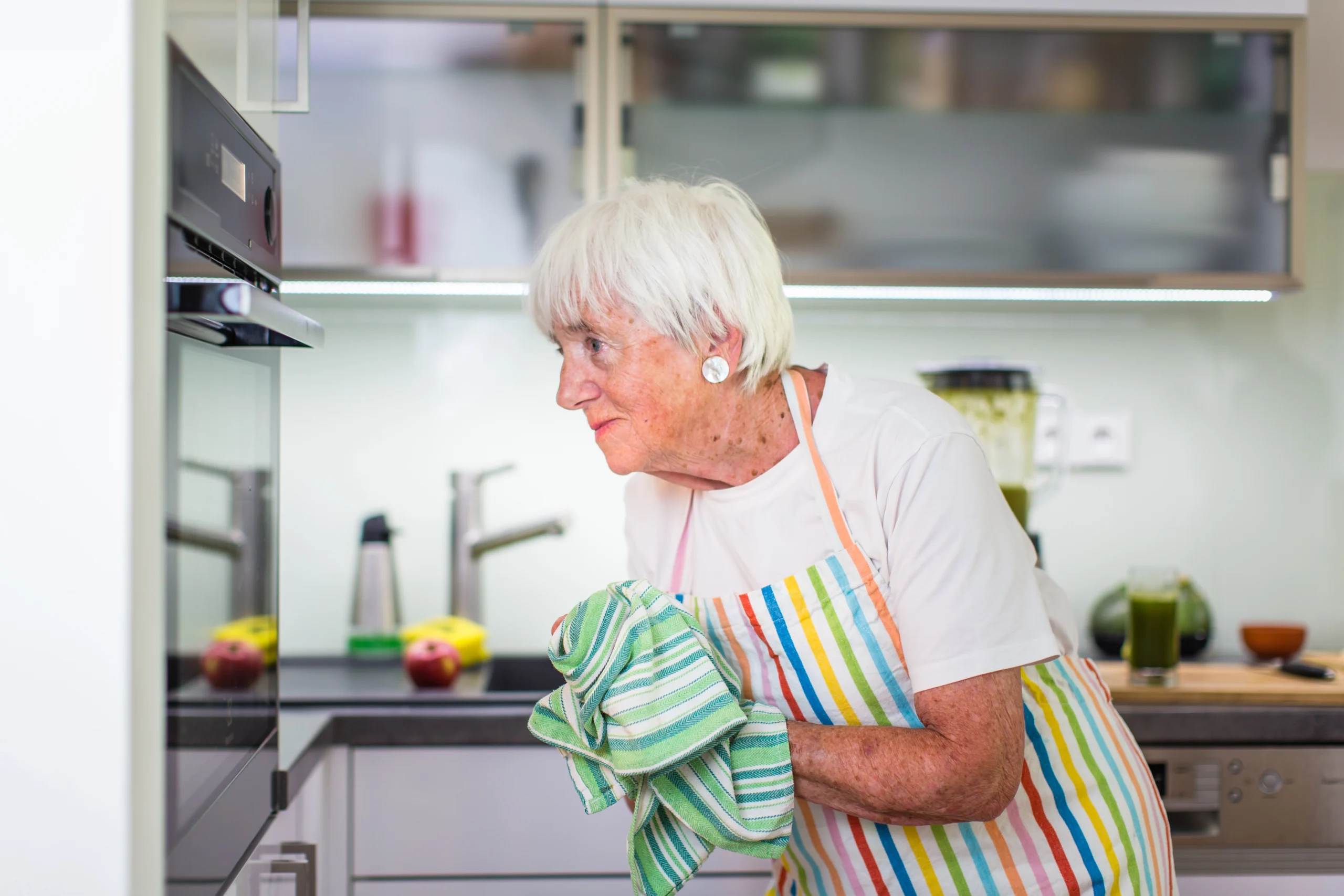 Babička kontroluje jídlo v troubě. Usmívající se spokojená starší žena v kuchyni 