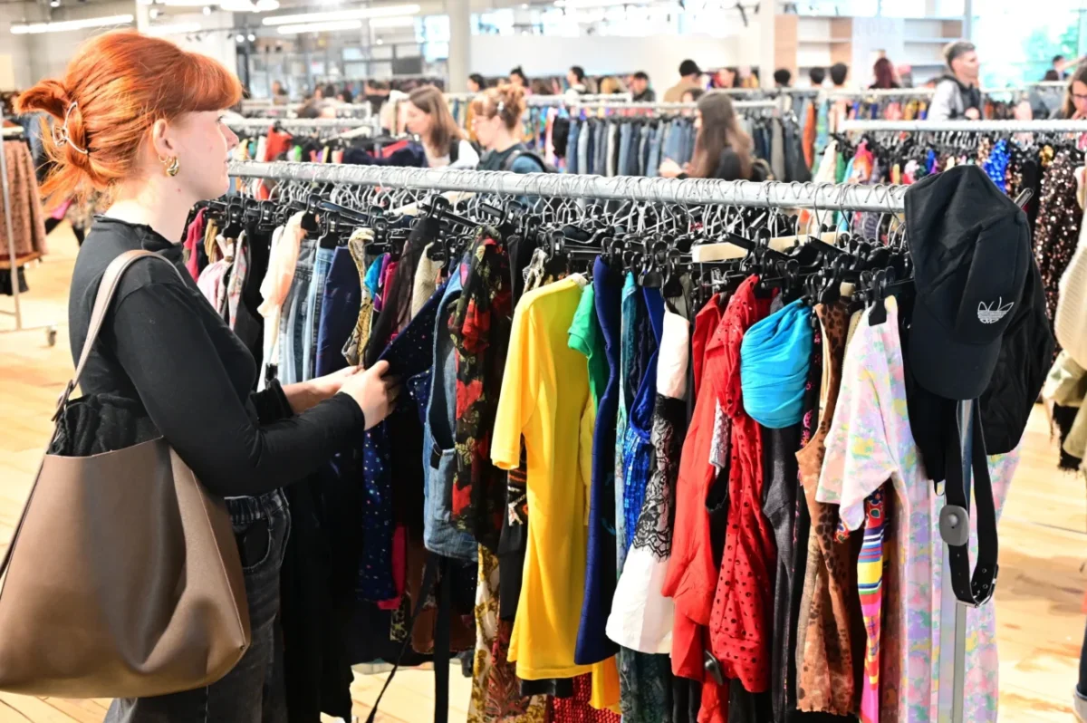 Žena si projíždí stojan s oblečením.