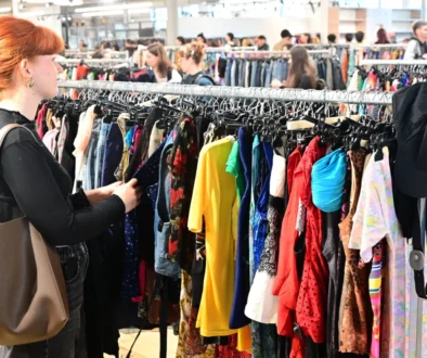 Žena si projíždí stojan s oblečením.