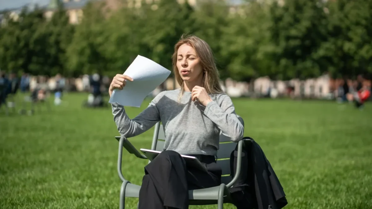 žena sedí venku, je jí horko, ovívá se