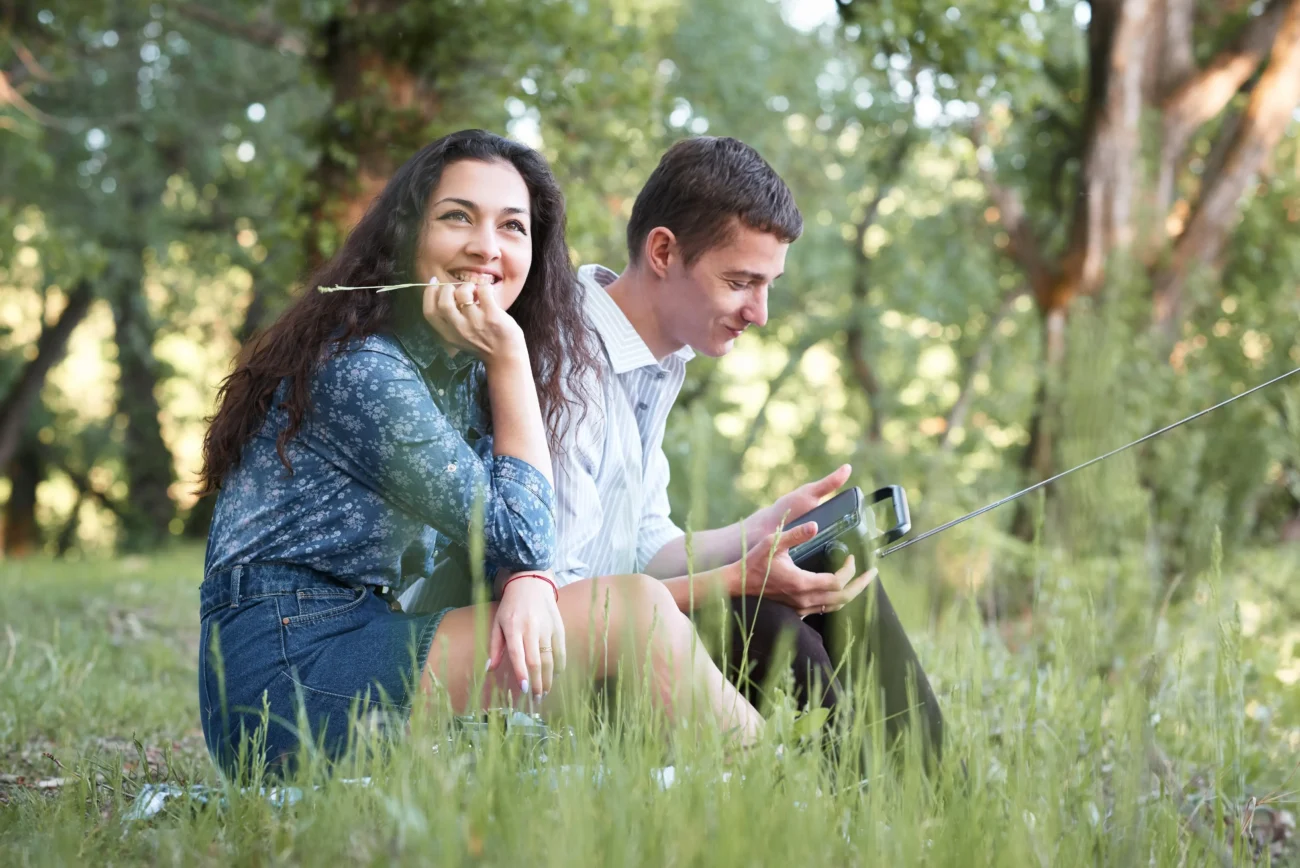 Lidé sedí v trávě a v ruce mají rádio. 
