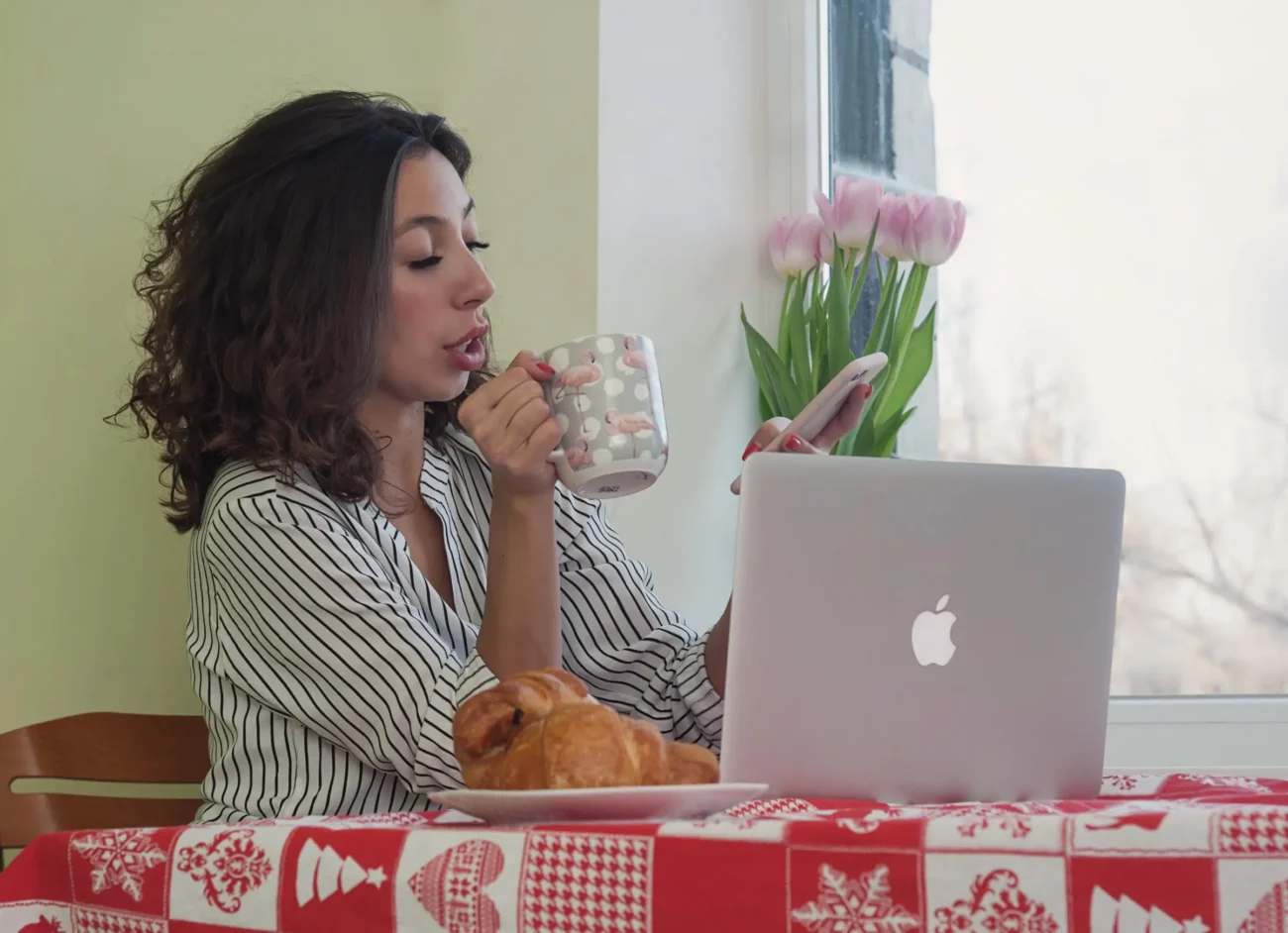 shutterstock_2079490432-2 | TVGURU.cz Žena sedí u stolu a dívá se do telefonu.