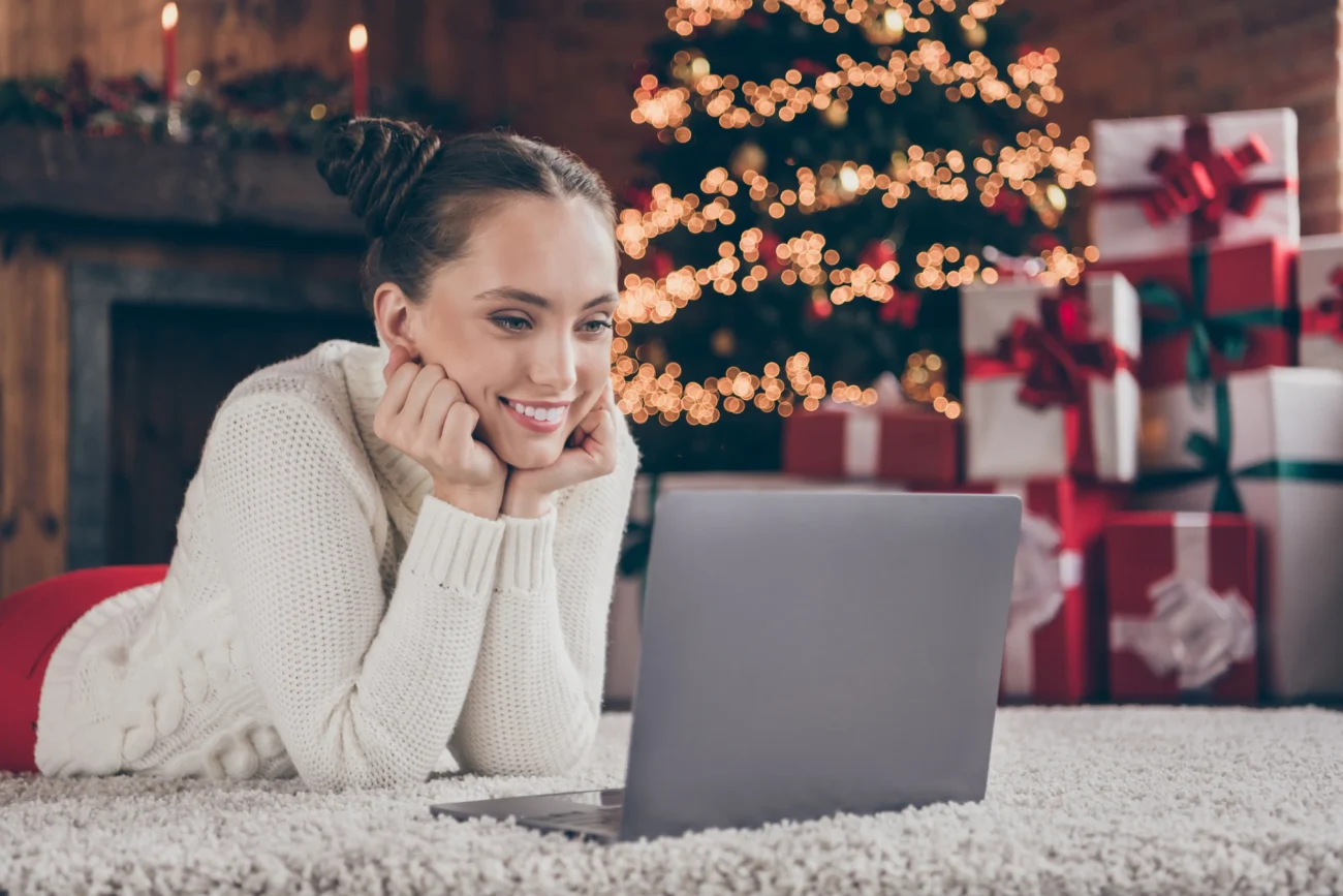 shutterstock_2053134605 1 | TVGURU.cz Žena leží na zemi u notebooku s vánočním stromečkem v pozadí.