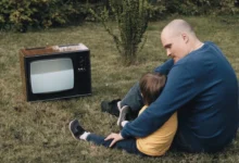 Muž s chlapcem sedí na zemi u televize.