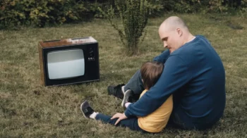 Muž s chlapcem sedí na zemi u televize.