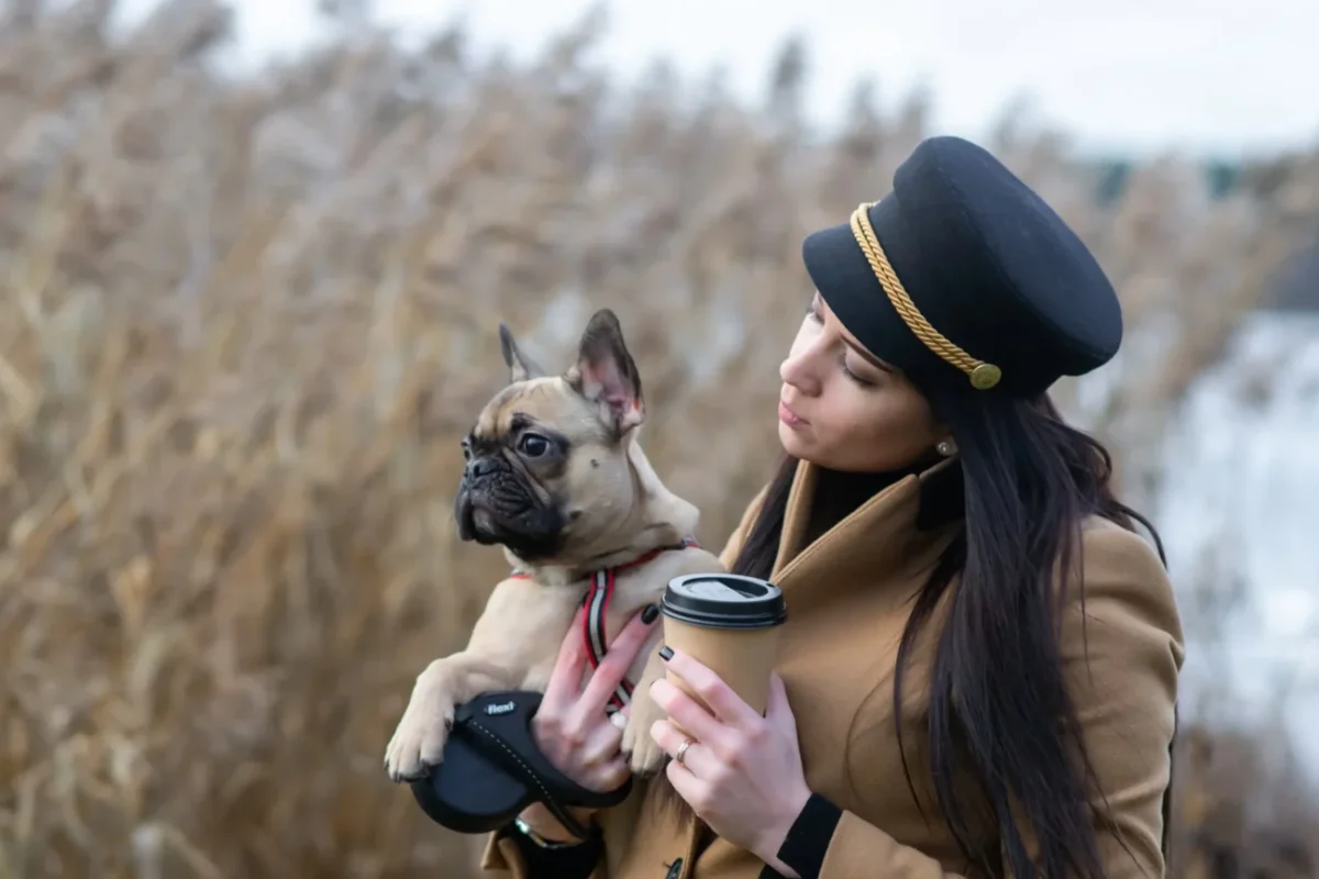 Žena v ruce drží kávu a pejska.