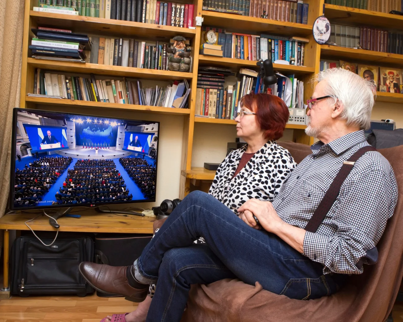 Starší pár sedí na gauči a dívá se na televizi. 