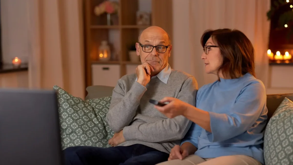 Pán s paní sedí na gauči a sledují televizi.