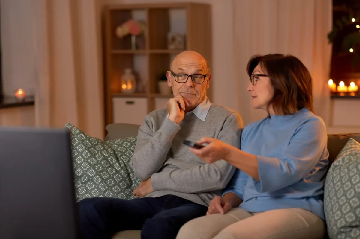 Pán s paní sedí na gauči a sledují televizi.