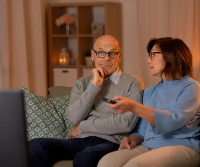 Pán s paní sedí na gauči a sledují televizi.