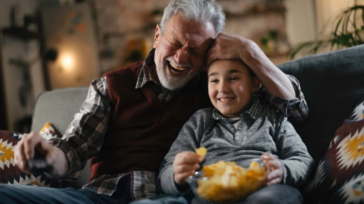 Starý pán s chlapcem sedí na gauči a smějí se.