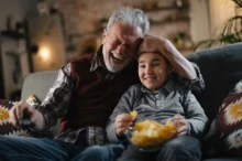 Starý pán s chlapcem sedí na gauči a smějí se.