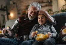 Starý pán s chlapcem sedí na gauči a smějí se.