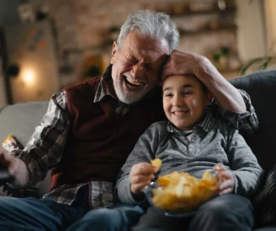 Starý pán s chlapcem sedí na gauči a smějí se.