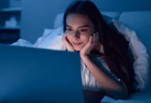 Žena leží u notebooku a usmívá se.