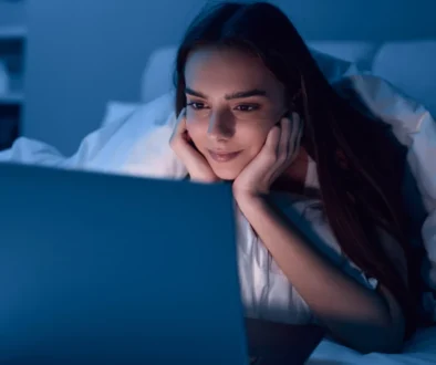 Žena leží u notebooku a usmívá se.