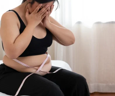 Mladá žena sedí na posteli s krejčovským metrem kolem břicha.