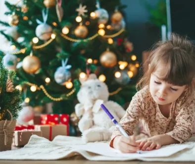Malá holčička píše dopis Ježíškovi u vánočního stromečku.