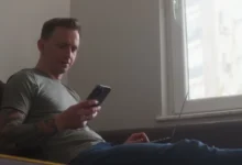 muž kouká do telefonu a počítače