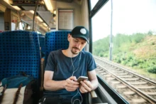 Mladý muž cestuje vlakem a v uších má sluchátka.