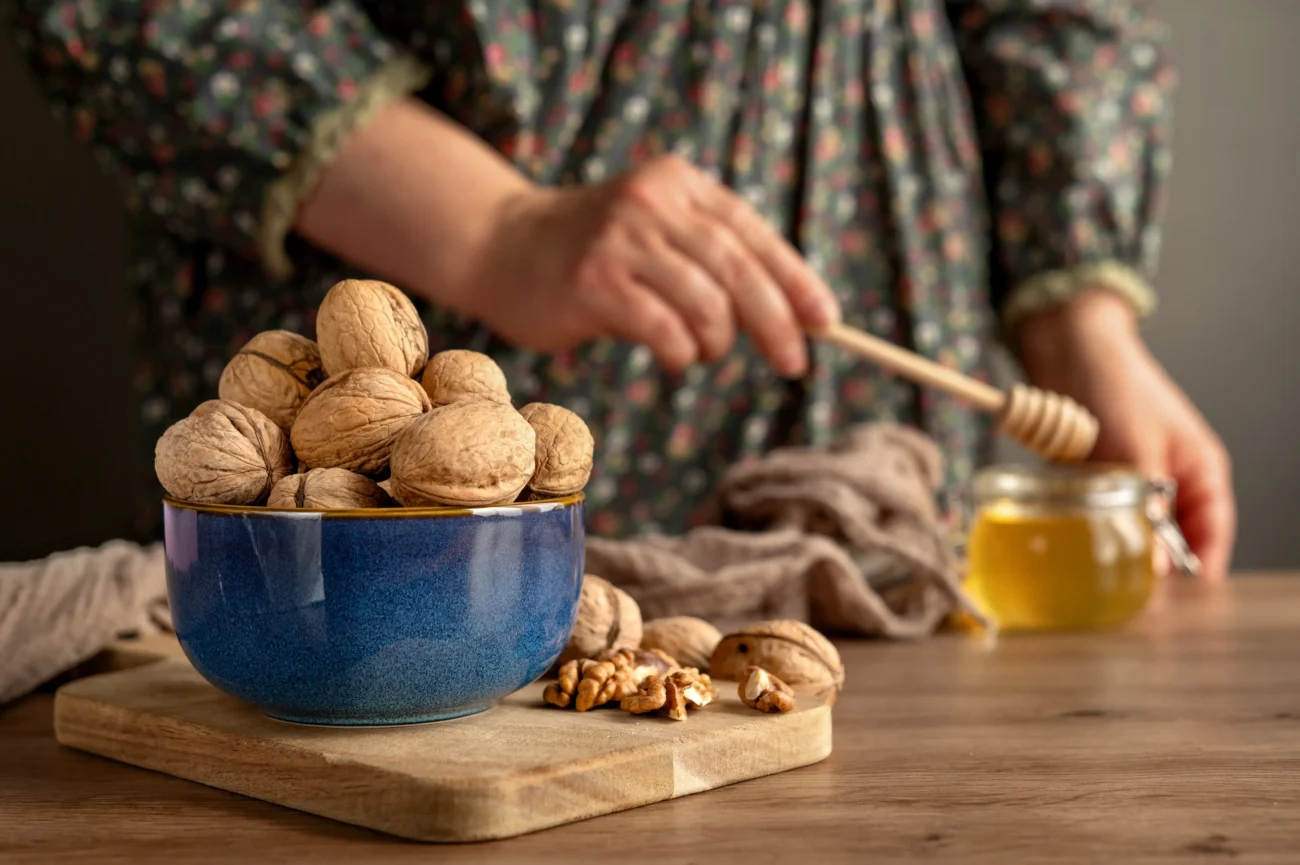 shutterstock_2685632401-2 | TVGURU.cz Žena stojí u medu a ořechů.
