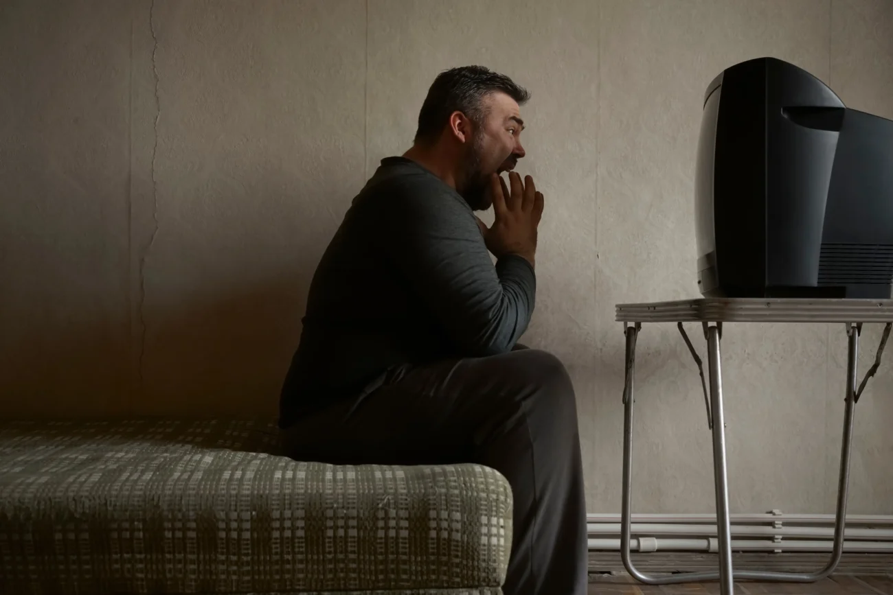 Muž sedí před starou televizí. 