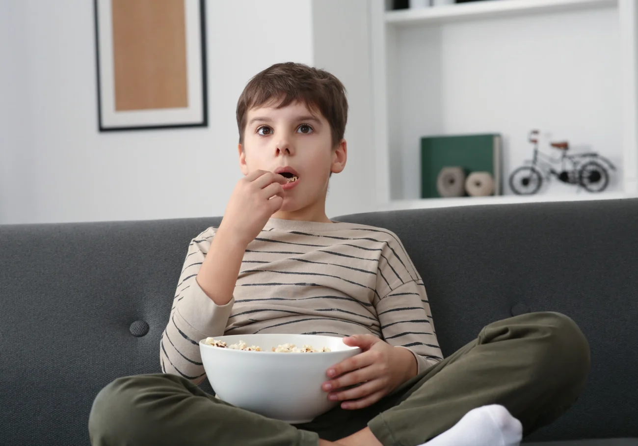 shutterstock_2340032873 1 | TVGURU.cz Malý kluk sedí s popcornem před televizí.