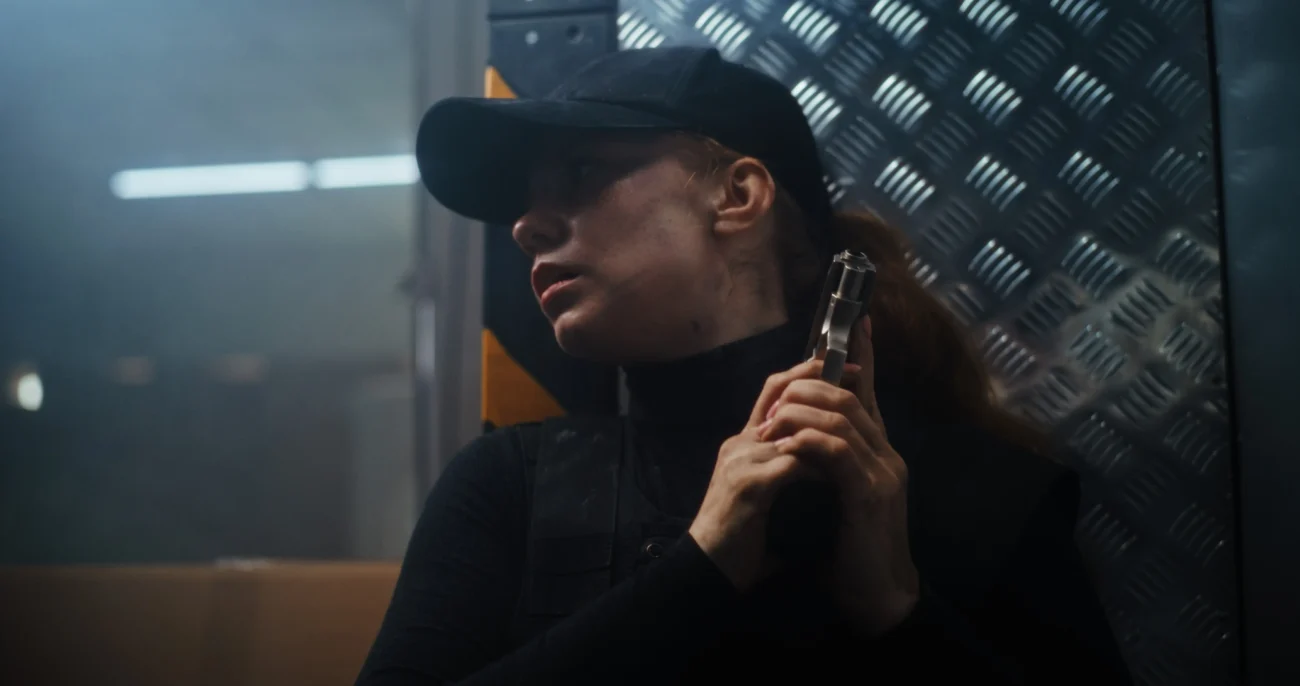 Žena v černém oblečení s pistolí. 