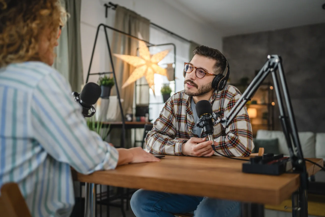 Dva lidé natáčí podcast u stolu. 