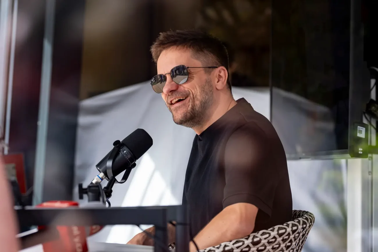 Jiří Mádl sedí na židli a usmívá se.