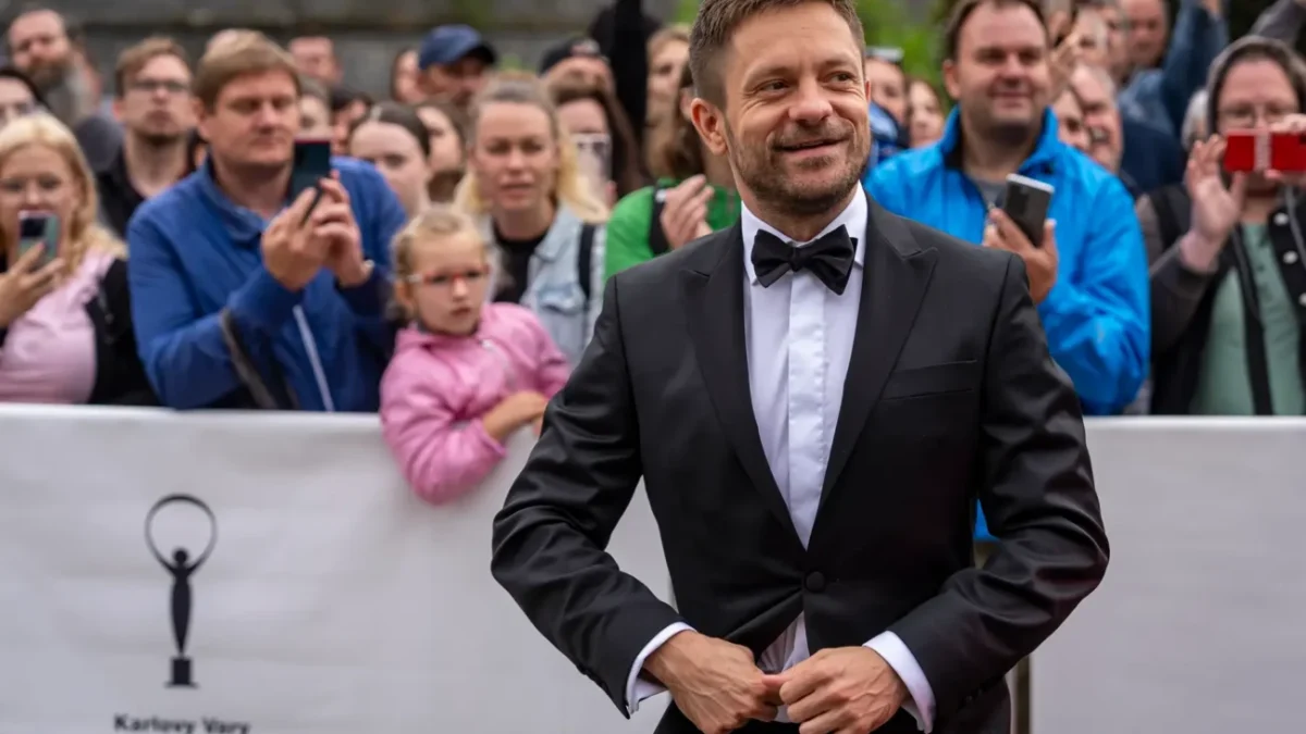 Jiří Mádl stojí před lidmi a usmívá se.