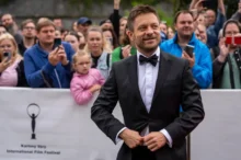 Jiří Mádl stojí před lidmi a usmívá se.