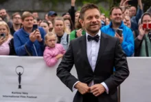 Jiří Mádl stojí před lidmi a usmívá se.