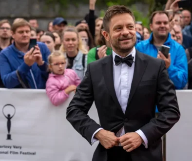 Jiří Mádl stojí před lidmi a usmívá se.