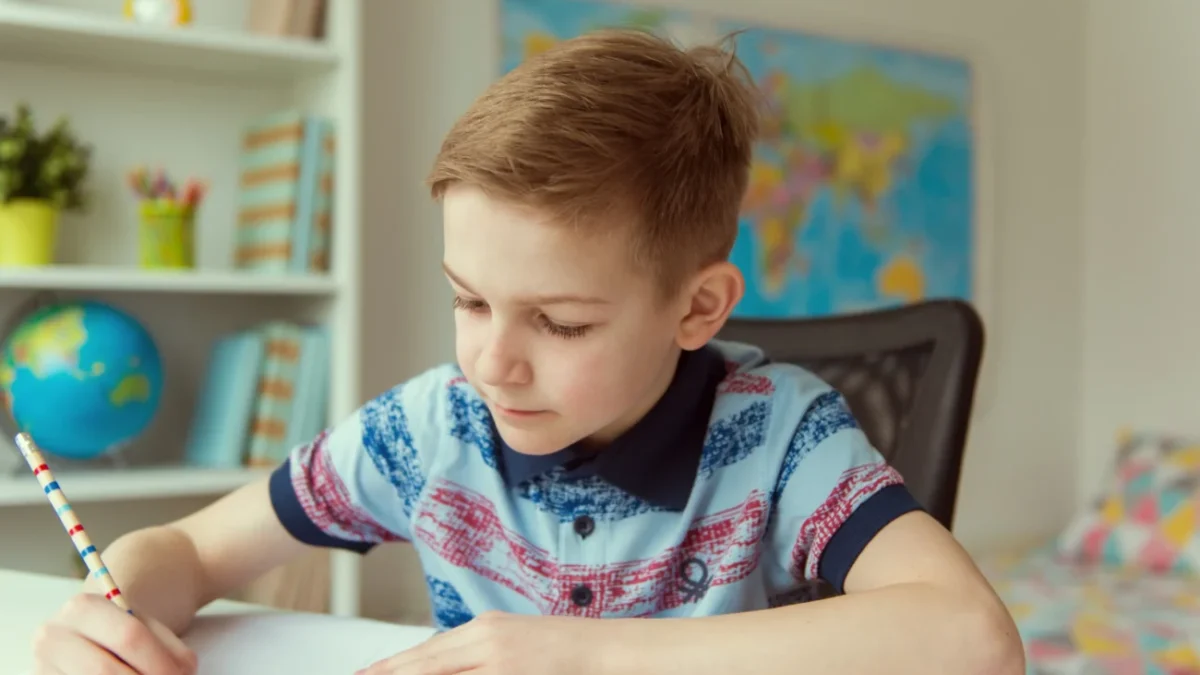 Chlapeček sedí u stolu a píše.