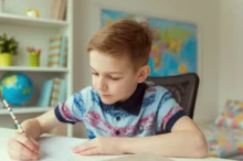 Chlapeček sedí u stolu a píše.