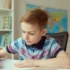 Chlapeček sedí u stolu a píše.