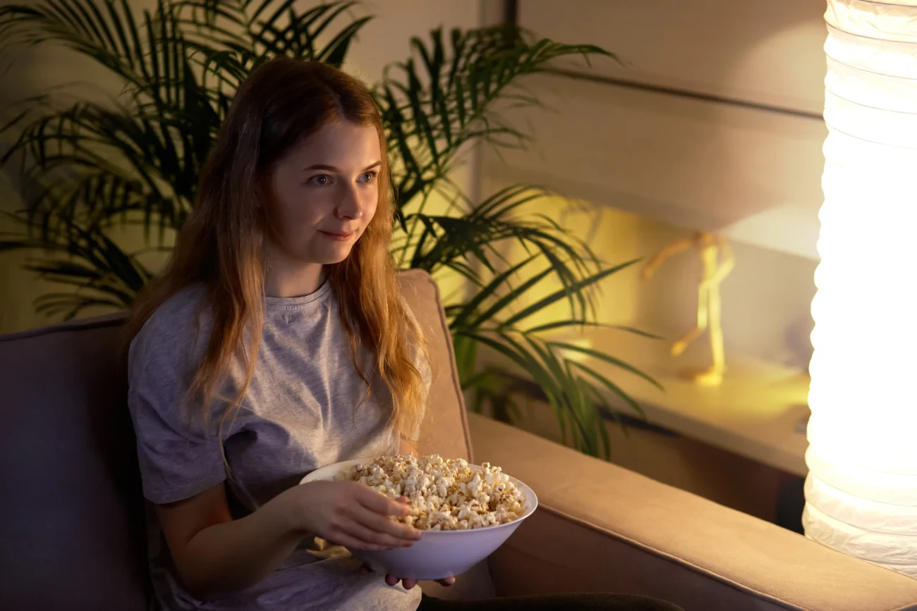 Žena sedí s mísou popcornu na gauči. 