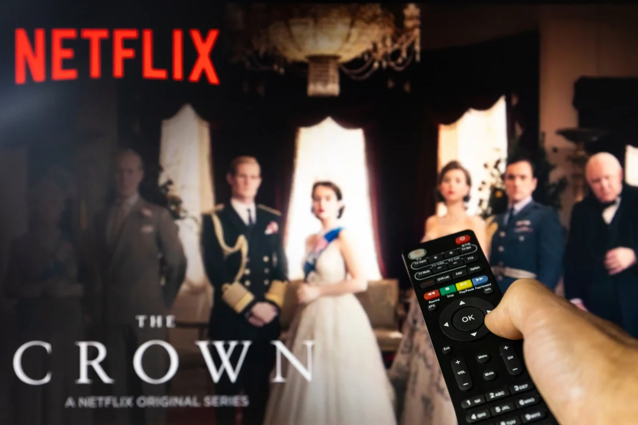 Člověk ovladačem míří na televizi, kde běží Koruna. 